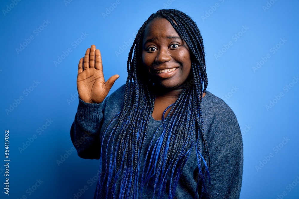 African american plus size woman with braids wearing casual sweater over blue background Waiving saying hello happy and smiling, friendly welcome gesture African american plus size woman with braids wearing casual sweater over blue background Waiving saying hello happy and smiling, friendly welcome gesture