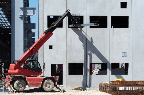 A telescopic handler, from exterior, brings up some steel bars to the first floor of the building under construction