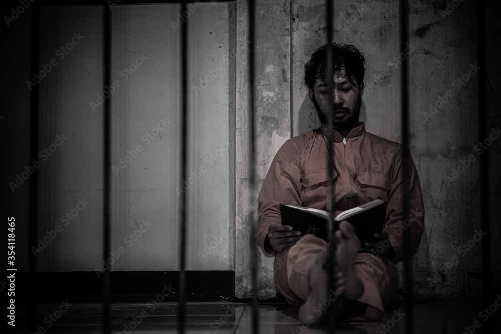 Asian man desperate at the iron prison,prisoner concept,thailand people,Hope to be free,Serious prisoners imprisoned in the prison,Reading a book