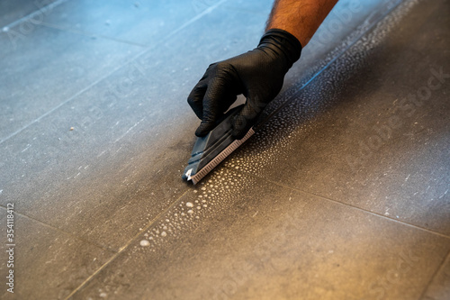 Foto professional cleaner cleaning grout with a brush blade and foamy soap on a gray