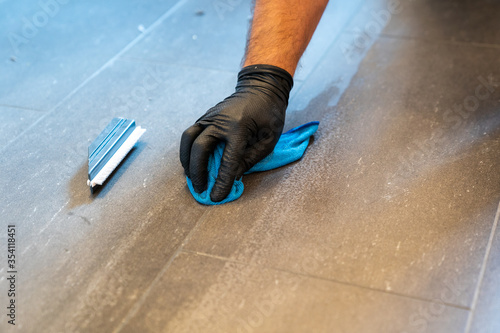 close up of professional cleaner cleaning grout with a blue cloth rag and foamy soap on a gray tiled bathroom floor