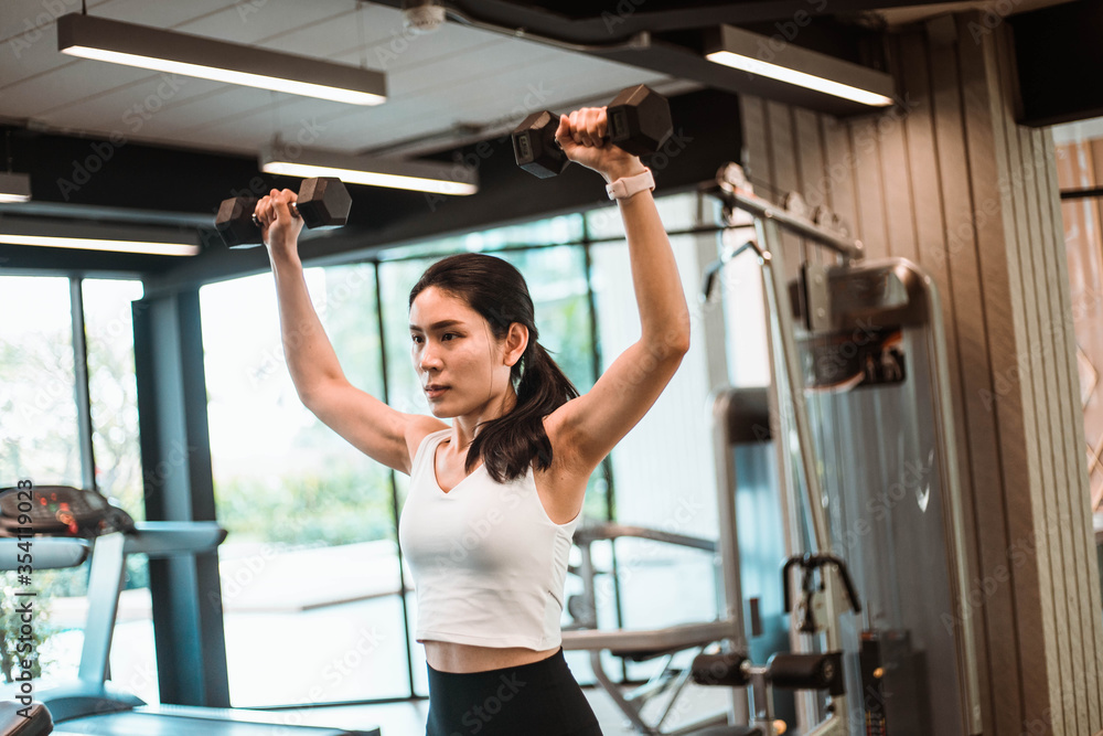 Fototapeta premium Young beautiful slim woman doing exercises with dumbbell in gym
