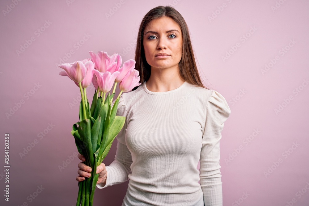 Young beautiful romantic woman with blue eyes holding beauty bouquet of pink tulips with a confident expression on smart face thinking serious