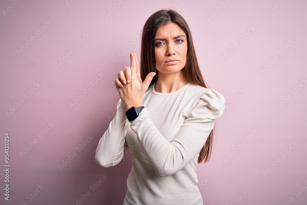 Young beautiful woman with blue eyes wearing casual white t-shirt over pink background Holding symbolic gun with hand gesture, playing killing shooting weapons, angry face Young beautiful woman with blue eyes wearing casual white t-shirt over pink background Holding symbolic gun with hand gesture, playing killing shooting weapons, angry face