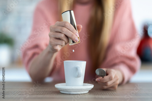 Tableau sur toile Woman hand throwing saccharin pills on coffee cup in the kitchen at home
