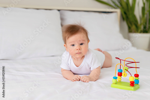 Newborn baby girl resting in bed. Family morning at home. Infant lies on his stomach in bed with a toy.