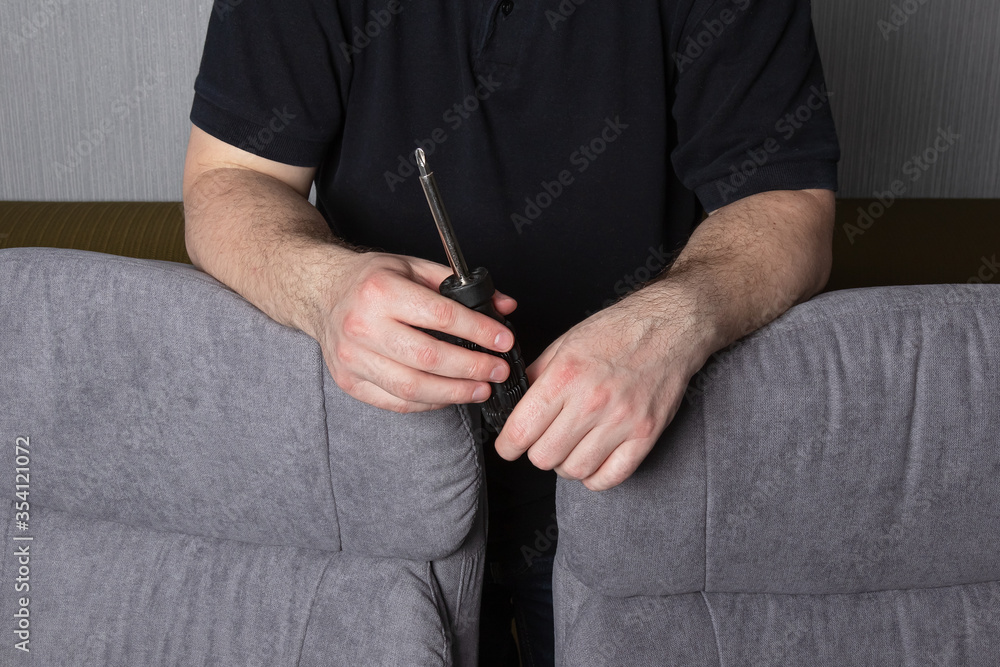 screwdriver in the hands of a man and two assembled chairs at home. Assembly concept.