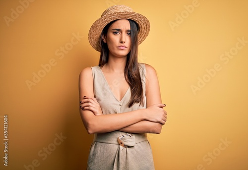 Young beautiful brunette woman on vacation wearing casual dress and hat skeptic and nervous, disapproving expression on face with crossed arms. Negative person.