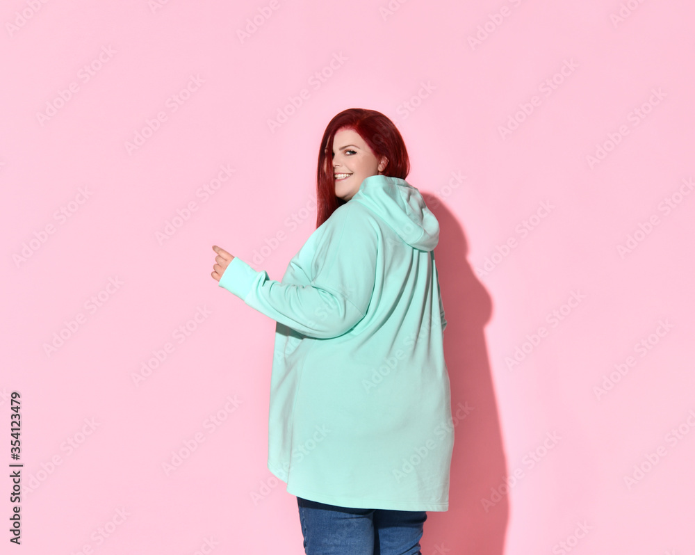 Fototapeta premium Adorable overweight lady turning sideways to camera holding hand on waist. Three quarter length shot isolated on pink, copy space