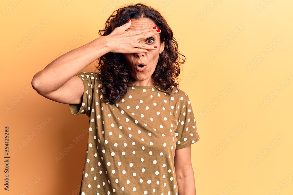 Middle age beautiful woman wearing casual t shirt peeking in shock covering face and eyes with hand, looking through fingers afraid Middle age beautiful woman wearing casual t shirt peeking in shock covering face and eyes with hand, looking through fingers afraid