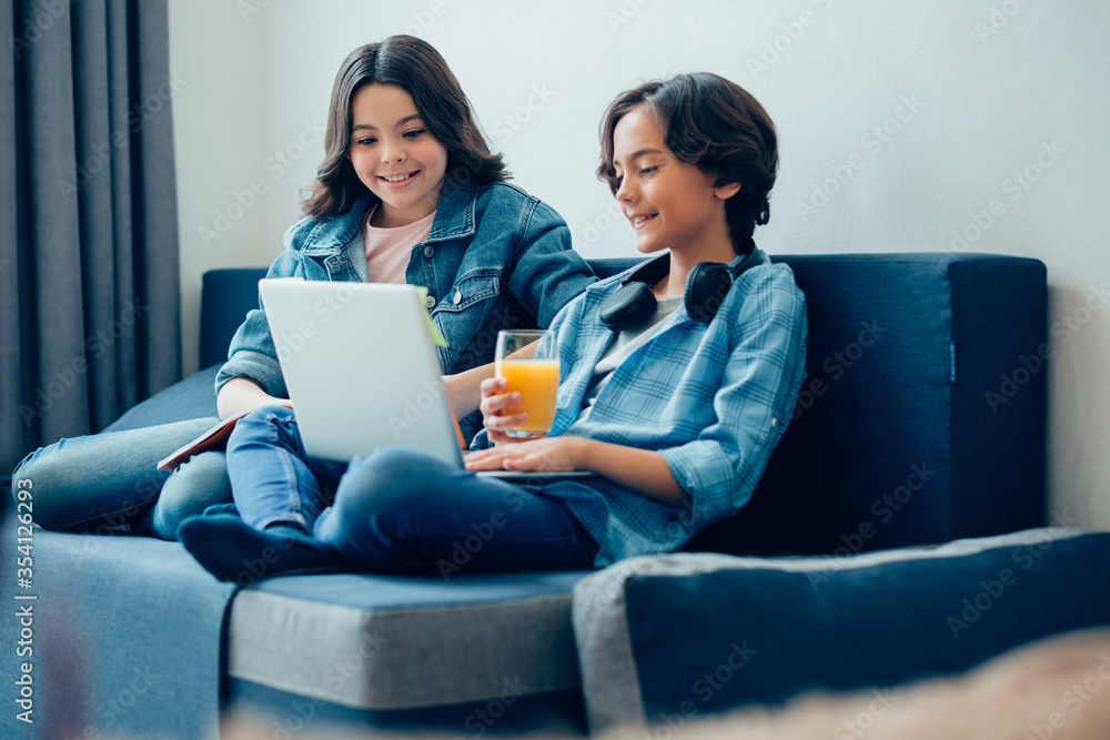 Mirthful children enjoying spending time online at home Mirthful children enjoying spending time online at home