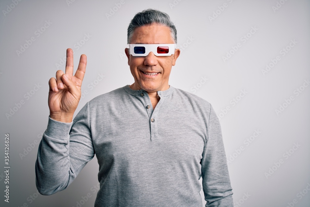 Middle age handsome grey-haired man using 3d glasses over isolated white background smiling with happy face winking at the camera doing victory sign. Number two. Middle age handsome grey-haired man using 3d glasses over isolated white background smiling with happy face winking at the camera doing victory sign. Number two.