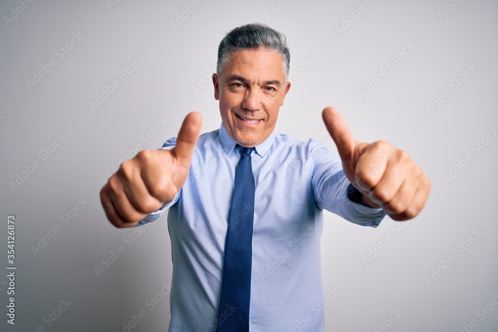 Middle age handsome grey-haired business man wearing elegant shirt and tie approving doing positive gesture with hand, thumbs up smiling and happy for success. Winner gesture. Middle age handsome grey-haired business man wearing elegant shirt and tie approving doing positive gesture with hand, thumbs up smiling and happy for success. Winner gesture.