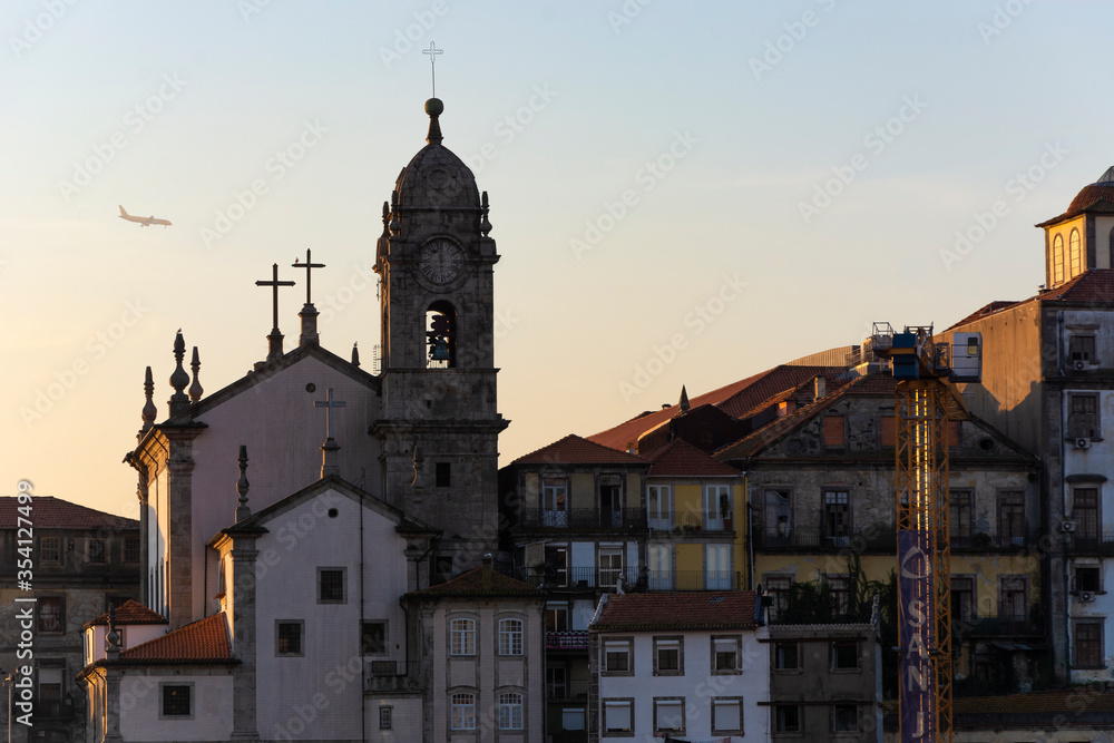 View to the Paroquial de Nossa Senhora da Vitória church. Plane preparing for landing in the background. Sunset. Porto, Portugal