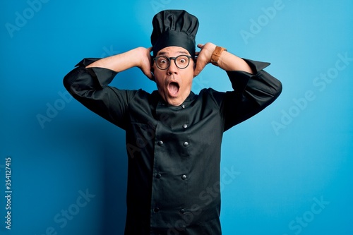 Middle age handsome grey-haired chef man wearing cooker uniform and hat Crazy and scared with hands on head, afraid and surprised of shock with open mouth