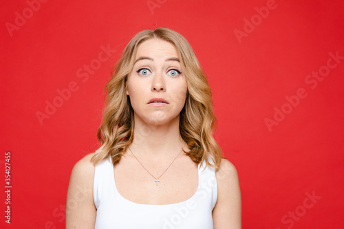 Young beautiful caucasian woman with medium fair wavy hair and nude makeup in white t-shirt fears, picture isolated on red background