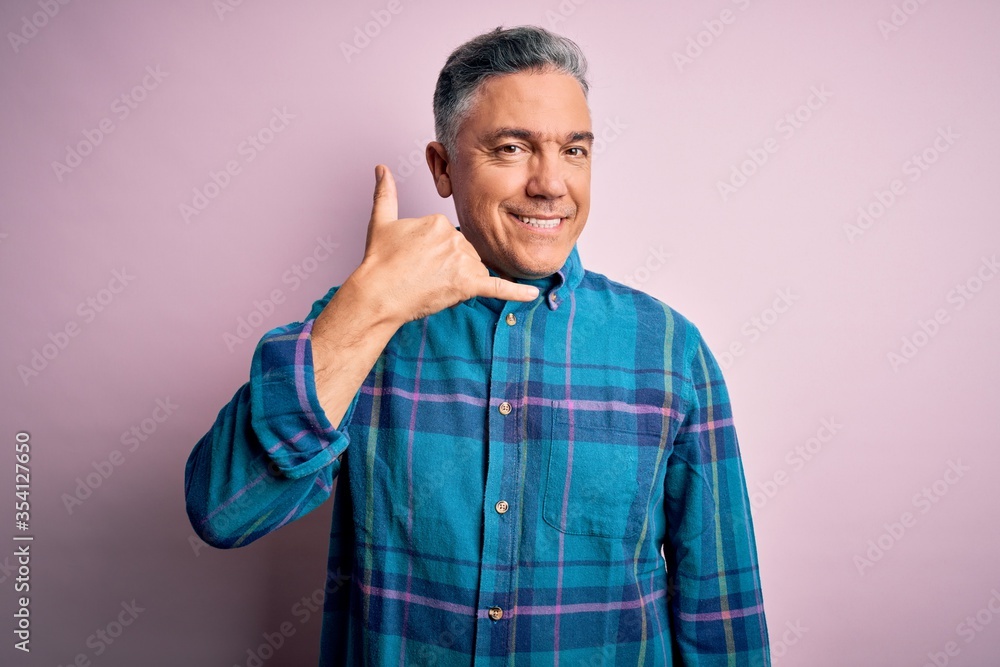 Middle age handsome grey-haired man wearing casual shirt over isolated pink background smiling doing phone gesture with hand and fingers like talking on the telephone. Communicating concepts. Middle age handsome grey-haired man wearing casual shirt over isolated pink background smiling doing phone gesture with hand and fingers like talking on the telephone. Communicating concepts.
