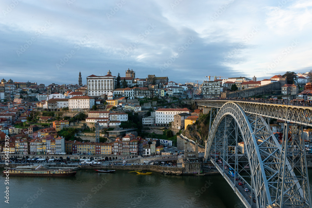Porto (Portugal) view, with Dom Luís Bridge and metro. Sunset, cloudy sky. Boats on the river.