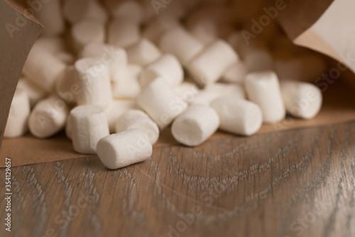 small white marshmallows spilling from paper bag on wooden background