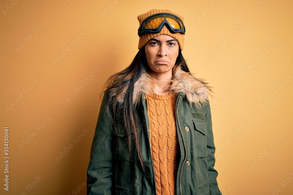 Young beautiful hispanic woman wearing ski glasses and coat for winter weather depressed and worry for distress, crying angry and afraid. Sad expression. Young beautiful hispanic woman wearing ski glasses and coat for winter weather depressed and worry for distress, crying angry and afraid. Sad expression.