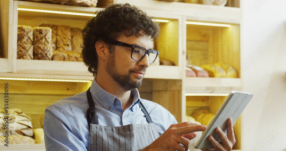Fototapeta premium Portrait of male baker working in bakery shop and using tablet