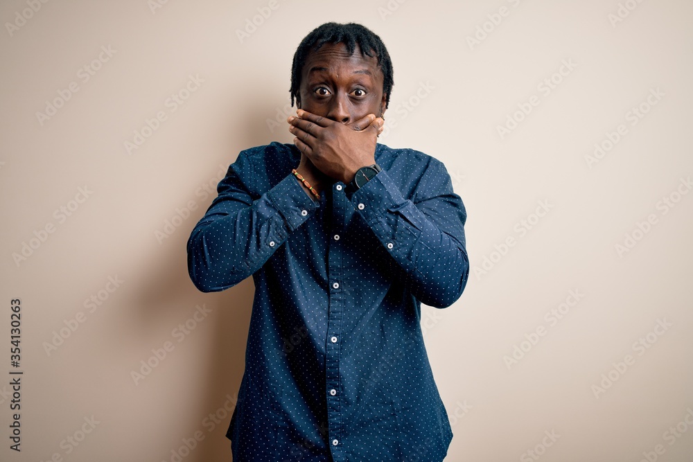 Young handsome african american man wearing casual shirt standing over white background shocked covering mouth with hands for mistake. Secret concept. Young handsome african american man wearing casual shirt standing over white background shocked covering mouth with hands for mistake. Secret concept.
