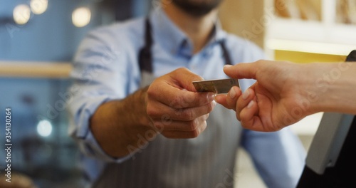 Close up of the female hands of the buyer giving a credit card for paying to the male vendor in the bakery shop. Indoor