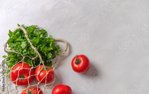 Eco bag of  tomatoes and bunch of fresh parsley on a light background. Sustainable lifestyle. Copy space