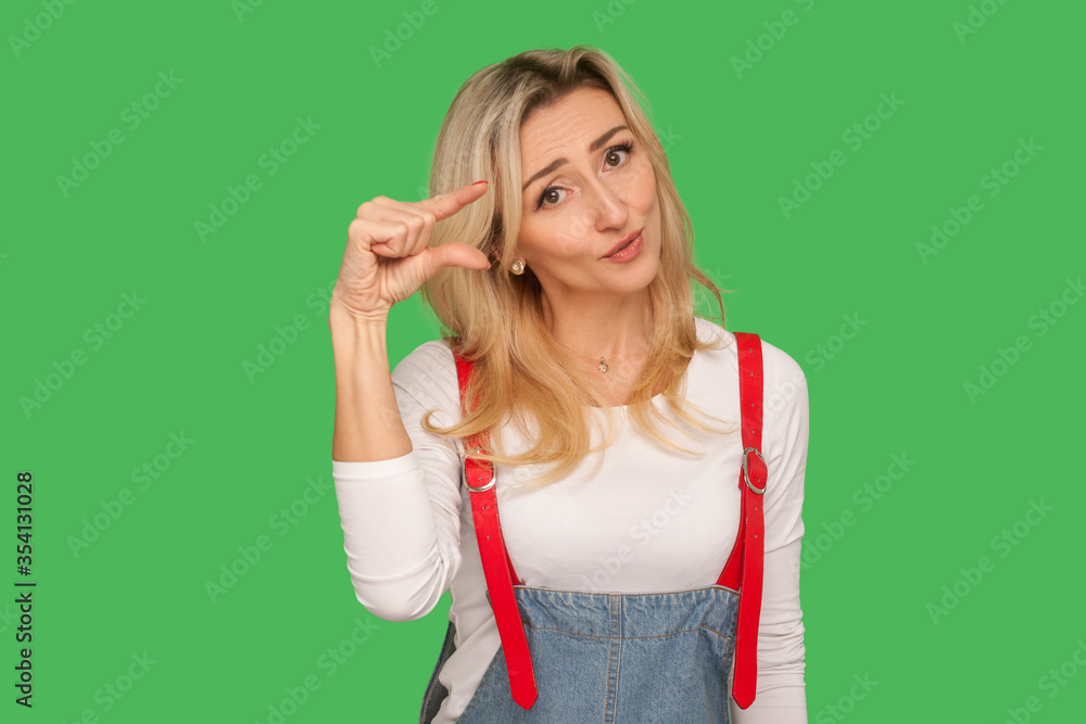Too small! Portrait of dissatisfied adult woman with apologizing look showing a little bit gesture, inch or centimeter, disappointed with minimum size. indoor studio shot isolated on green background Too small! Portrait of dissatisfied adult woman with apologizing look showing a little bit gesture, inch or centimeter, disappointed with minimum size. indoor studio shot isolated on green background
