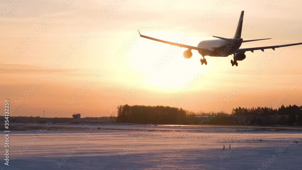 Silhouette of a passenger plane that lands at the airport at sunset in winter Silhouette of a passenger plane that lands at the airport at sunset in winter