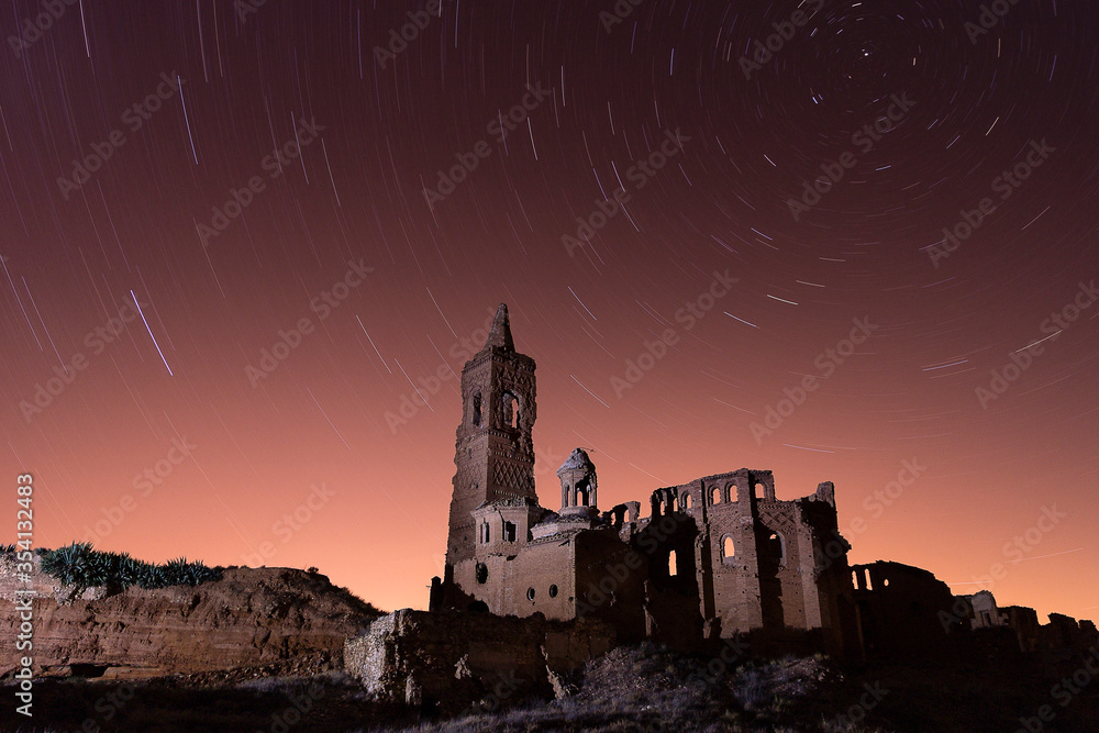 Obraz premium long exposure photography with circumpolar of the stars and lantern lighting of the church in the abandoned village of Belchite, Aragon, Spain