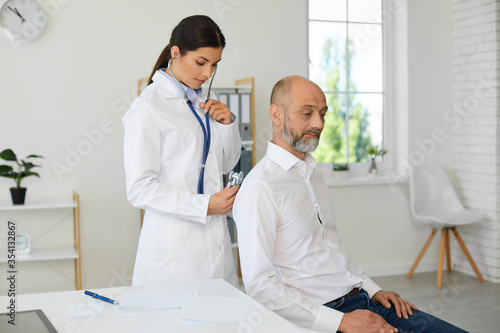 A female doctor with a stethoscope makes a diagnosis to a patient pensioner senior man in a modern hospital office.