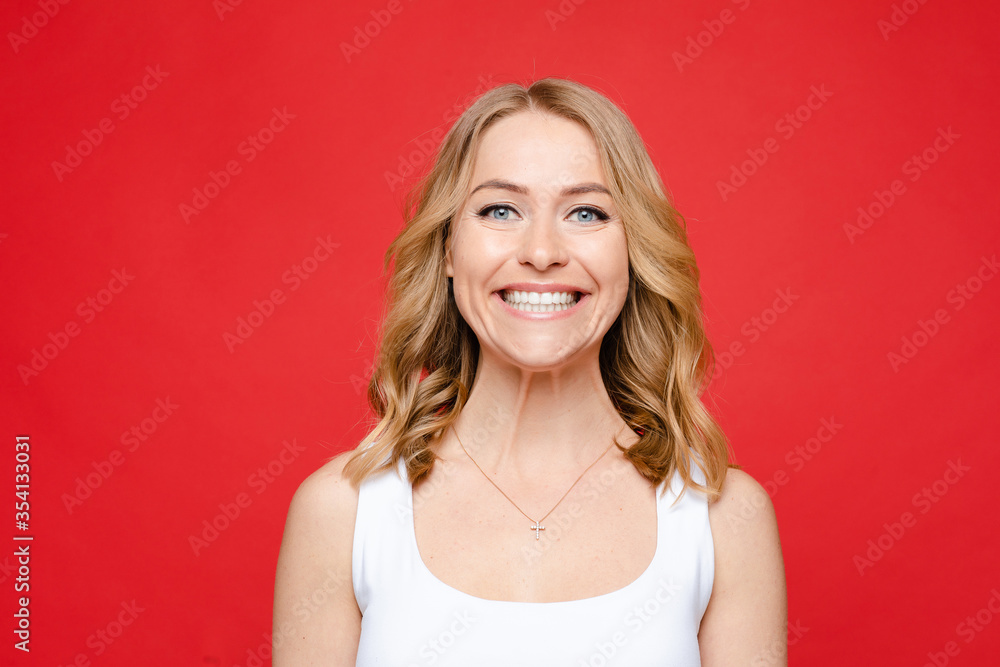 Young beautiful caucasian woman with medium fair wavy hair and nude makeup in white t-shirt rejoices, picture isolated on red background Young beautiful caucasian woman with medium fair wavy hair and nude makeup in white t-shirt rejoices, picture isolated on red background