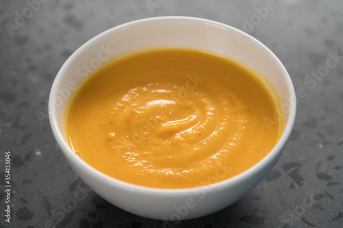 Pumpkin spicy soup puree in white bowl on concrete background