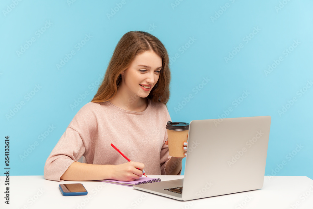 Woman drinking coffee, working on laptop and making notes on paper. Student studying, writing in notebook while listening online school, internet course. indoor studio shot isolated on blue background Woman drinking coffee, working on laptop and making notes on paper. Student studying, writing in notebook while listening online school, internet course. indoor studio shot isolated on blue background