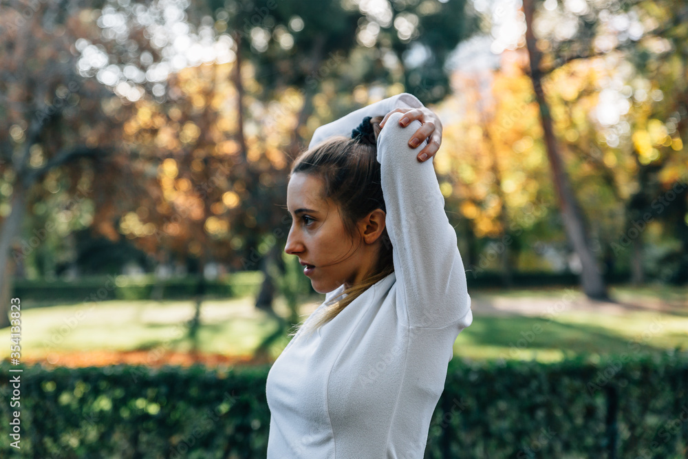 Side view of a young woman stretching her arms while doing sports in the middle of nature Side view of a young woman stretching her arms while doing sports in the middle of nature