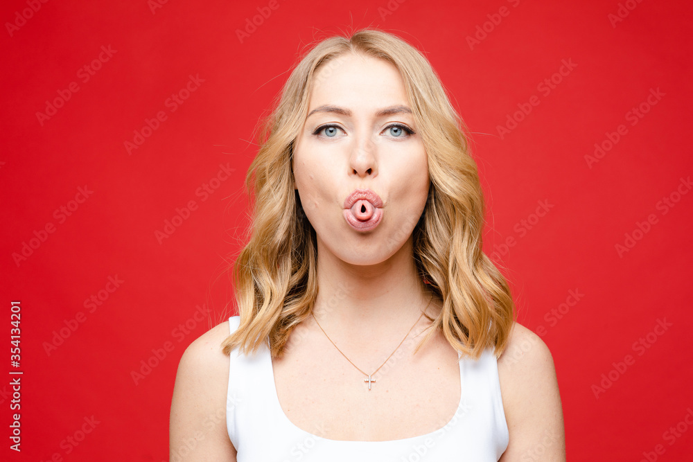 Young beautiful caucasian woman with medium fair wavy hair and nude makeup in white t-shirt is boring, picture isolated on red background Young beautiful caucasian woman with medium fair wavy hair and nude makeup in white t-shirt is boring, picture isolated on red background