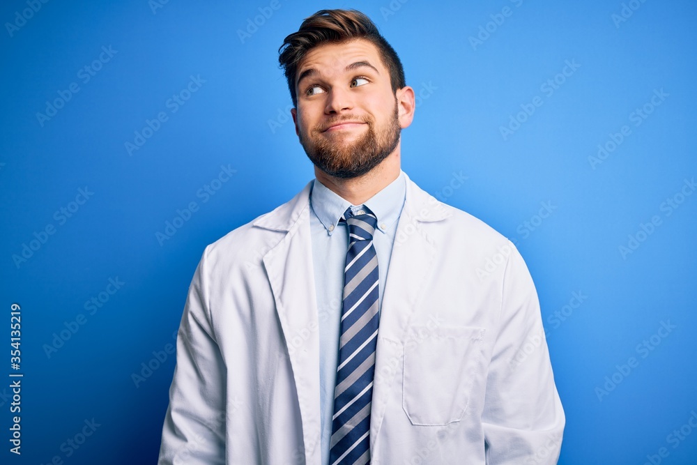 Young blond therapist man with beard and blue eyes wearing coat and tie over background smiling looking to the side and staring away thinking. Young blond therapist man with beard and blue eyes wearing coat and tie over background smiling looking to the side and staring away thinking.