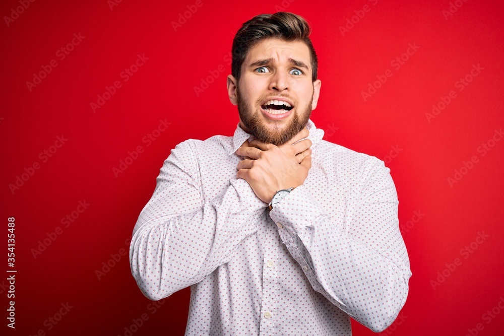Young blond businessman with beard and blue eyes wearing elegant shirt over red background shouting and suffocate because painful strangle. Health problem. Asphyxiate and suicide concept.