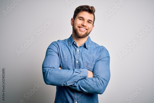 Young handsome blond man with beard and blue eyes wearing casual denim shirt happy face smiling with crossed arms looking at the camera. Positive person. © Krakenimages.com