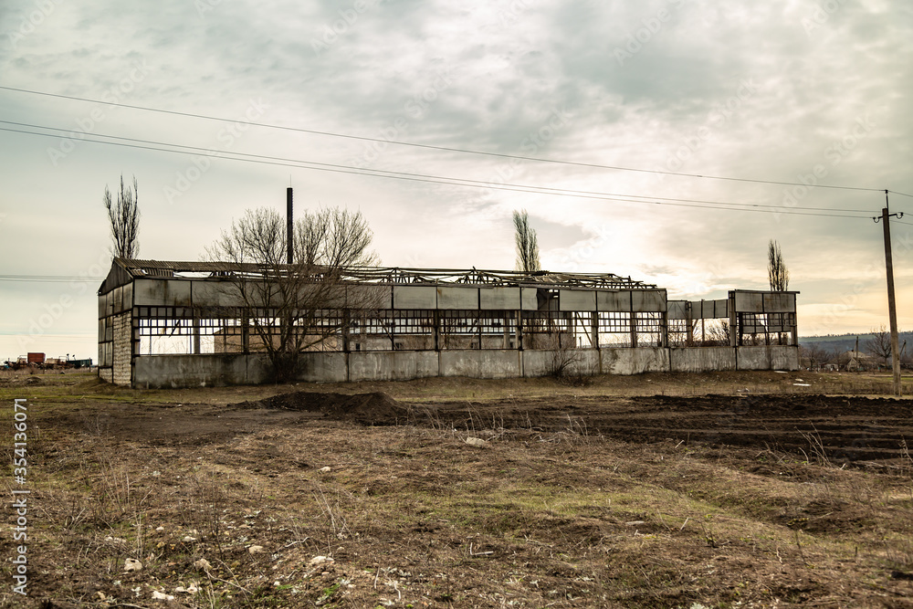 An abandoned dilapidated old empty cowshed building is in a field with dry grass. Outside view. Horizontal orientation. 