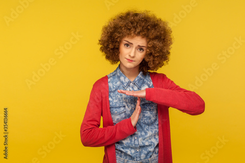 Please, need break! Portrait of unhappy pleading woman with curly hair looking tired, asking for pause with time out hand gesture, warning of deadline. indoor studio shot isolated on yellow background