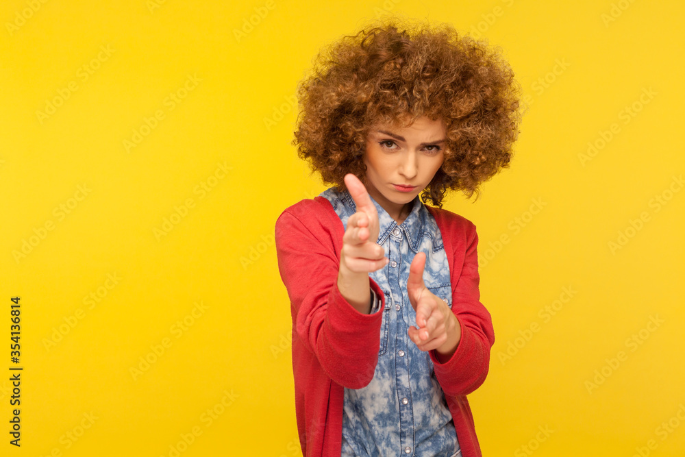 I'll kill you! Portrait of curly-haired hipster woman pointing finger guns to camera, aiming target and threatening to shoot with pistol hand gesture. indoor studio shot isolated on yellow background I'll kill you! Portrait of curly-haired hipster woman pointing finger guns to camera, aiming target and threatening to shoot with pistol hand gesture. indoor studio shot isolated on yellow background