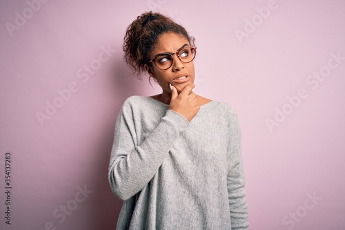 Young beautiful african american girl wearing sweater and glasses over pink background Thinking worried about a question, concerned and nervous with hand on chin