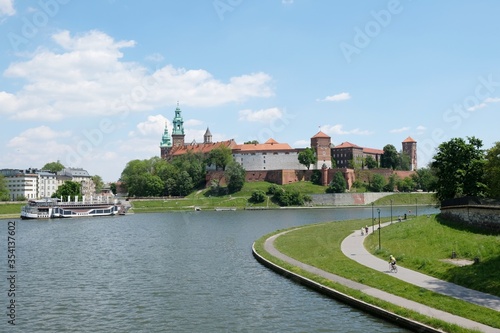Landscape with Vistula river and Wawel Royal Castlee. People walking and cycling along path by river on sunny summer day. Cracow, Poland.