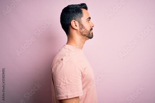 Young handsome man with beard wearing casual t-shirt standing over pink background looking to side, relax profile pose with natural face with confident smile. © Krakenimages.com