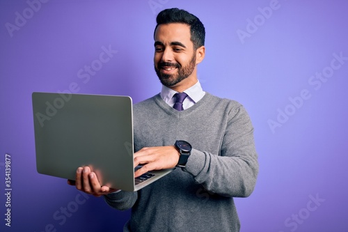 Young handsome businessman with beard working using laptop over purple background with a happy face standing and smiling with a confident smile showing teeth