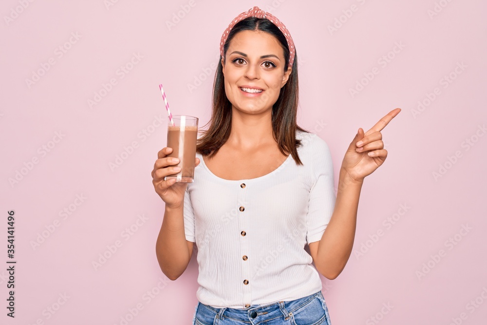 Young beautiful brunette woman drinking glass of chocolate beverage using straw Smiling happy pointing with hand and finger to the side Young beautiful brunette woman drinking glass of chocolate beverage using straw Smiling happy pointing with hand and finger to the side