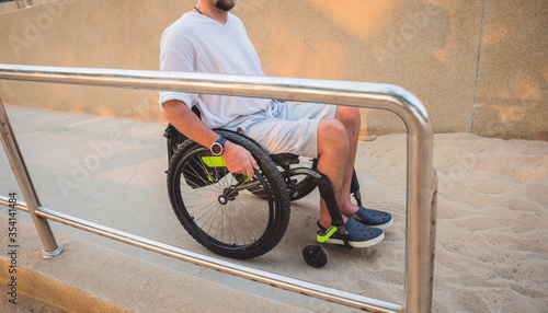 Disabled man in a wheelchair moves on a ramp to the beach.