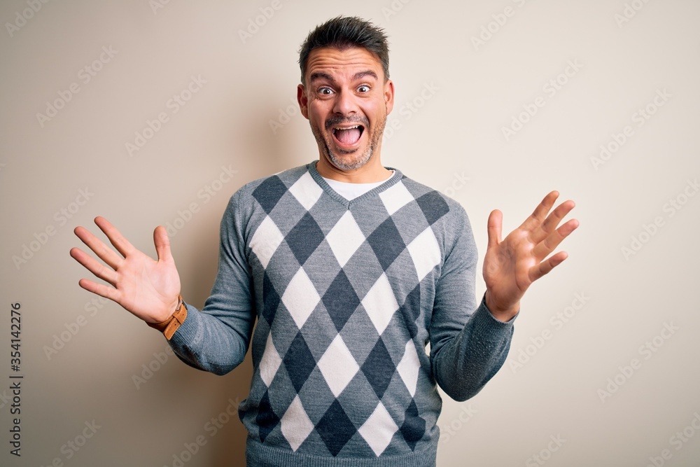 Young handsome man wearing casual sweater standing over isolated white background celebrating crazy and amazed for success with arms raised and open eyes screaming excited. Winner concept Young handsome man wearing casual sweater standing over isolated white background celebrating crazy and amazed for success with arms raised and open eyes screaming excited. Winner concept